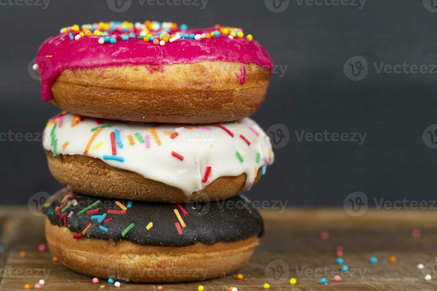 Lovely sweet food. Stack of glazed colorful assorted donuts with splashes on a gray background. photo