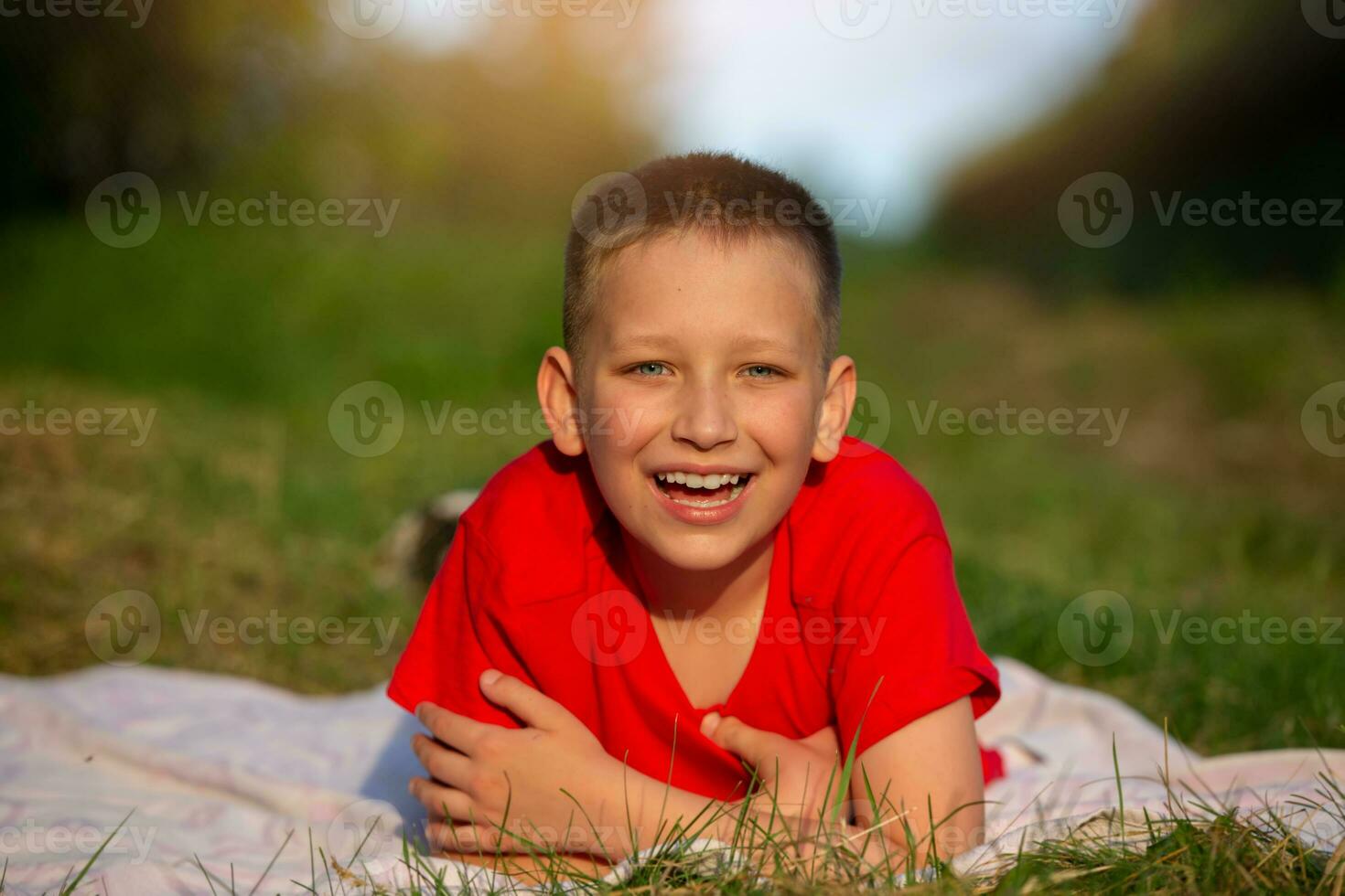 Happy boy lies on the grass smiling, looking at the camera. photo