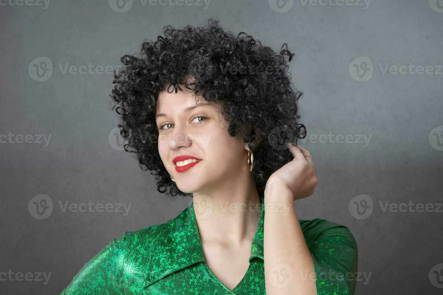 Vintage woman in afro wig and red disco costume on a gray background. Girl in the style of the seventies. photo