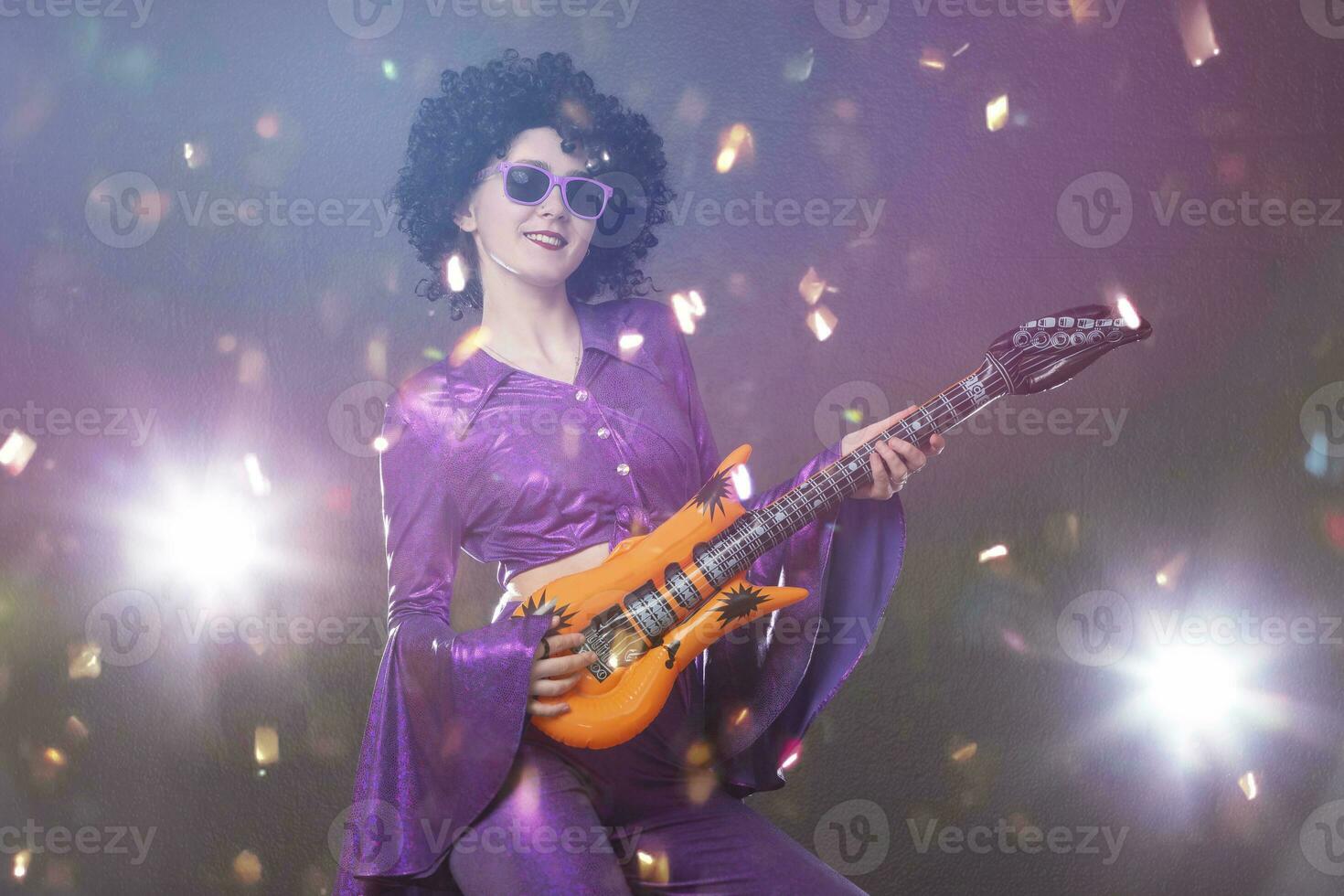 Happy girl pop singer with a toy guitar on the background of shiny confetti. Disco style. photo