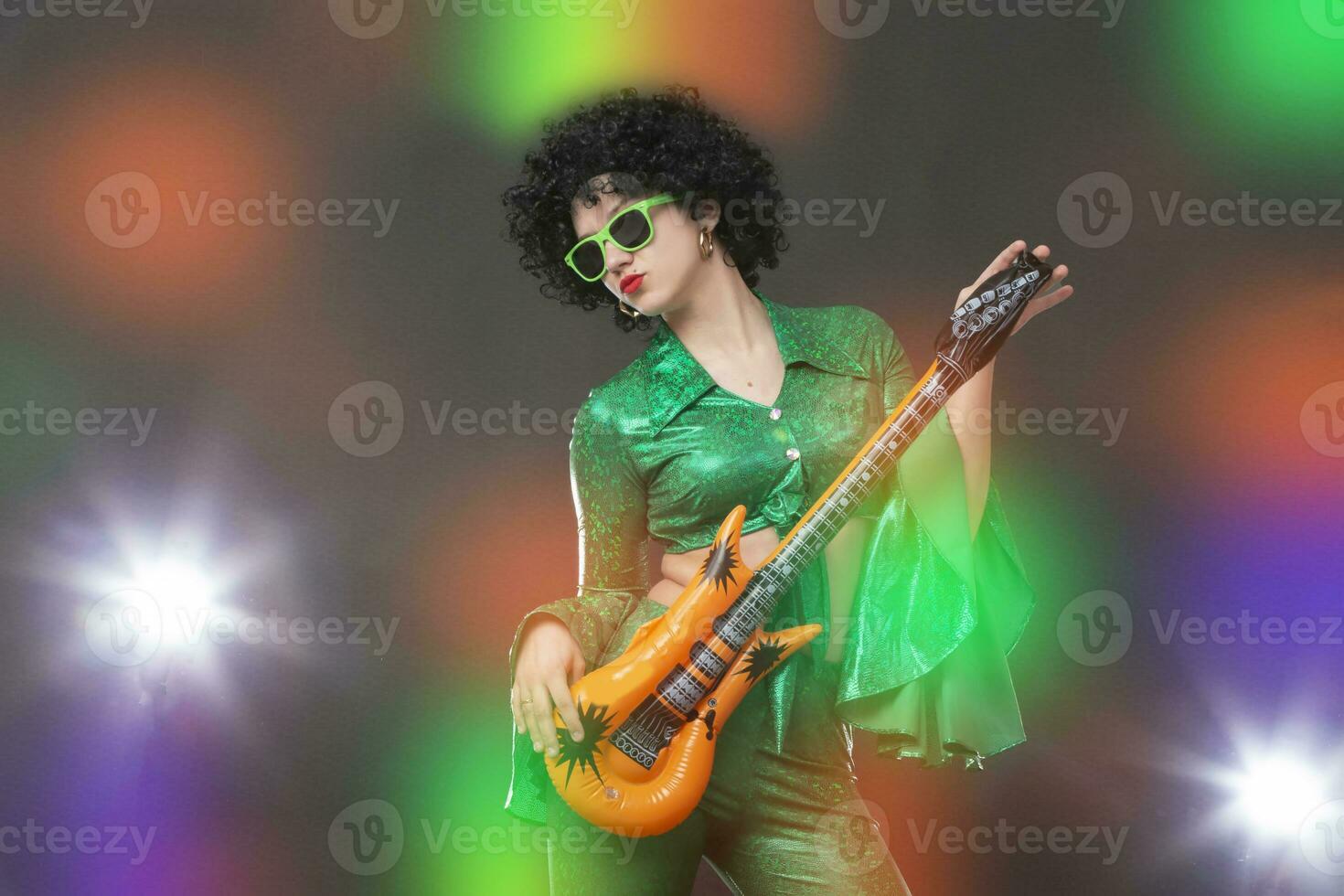 Retro disco woman with comic guitar posing against colorful stage lights. photo