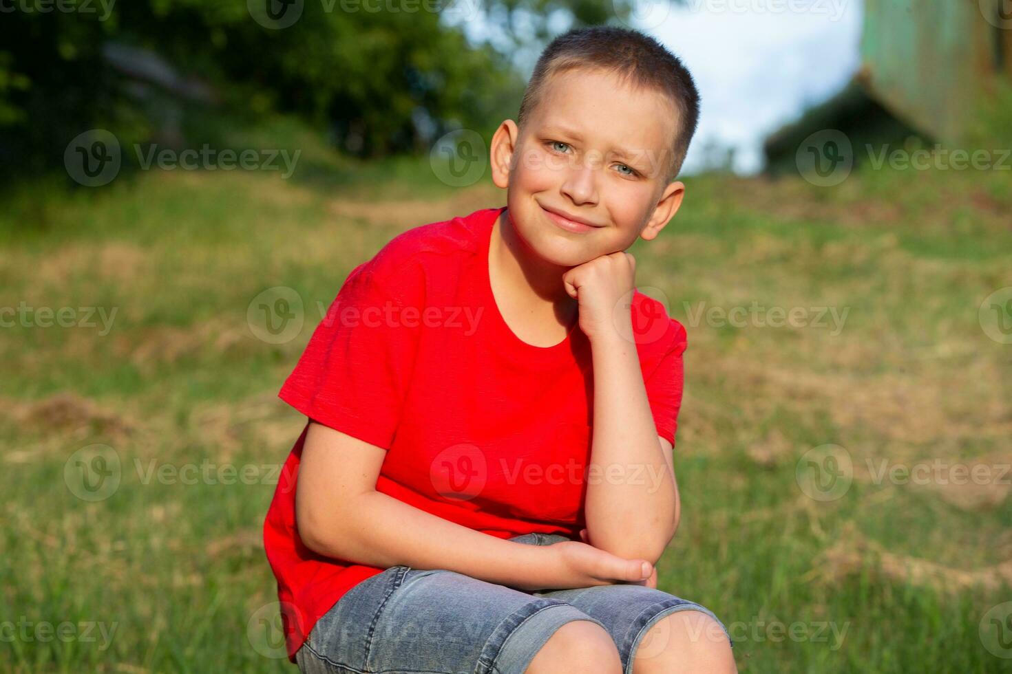 Portrait of an eight-year-old blond boy with blue eyes against the backdrop of a summer park. photo