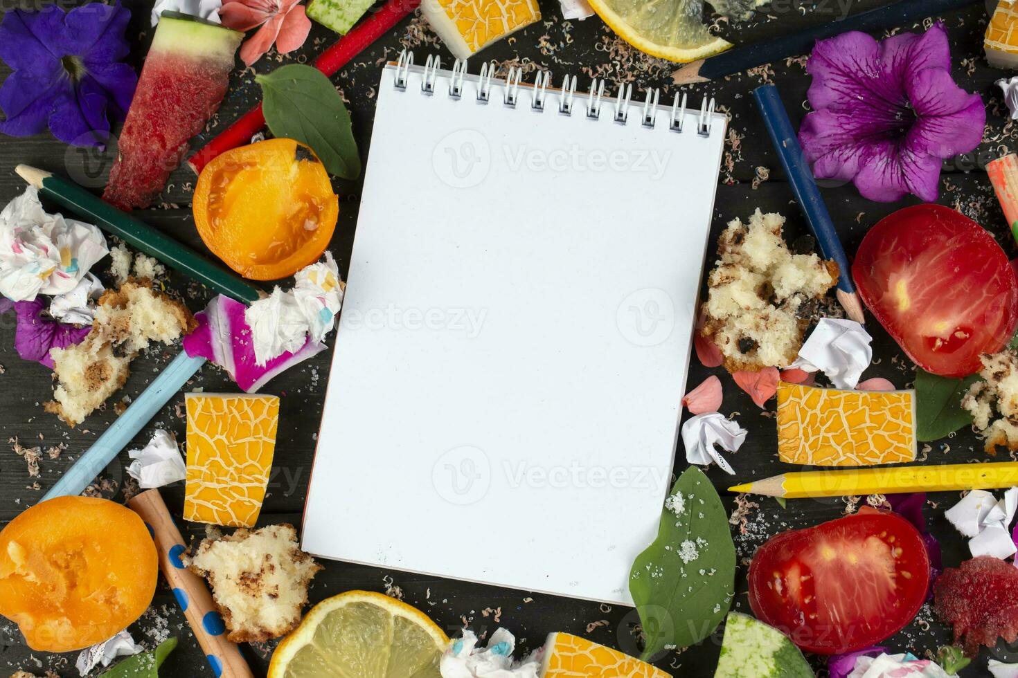 Paper notebook with blank pages, crumpled paper balls and crayons, scattered foods on wooden background, creative cooking recipe writing concept. Coming up and writing down recipes for cooking. photo