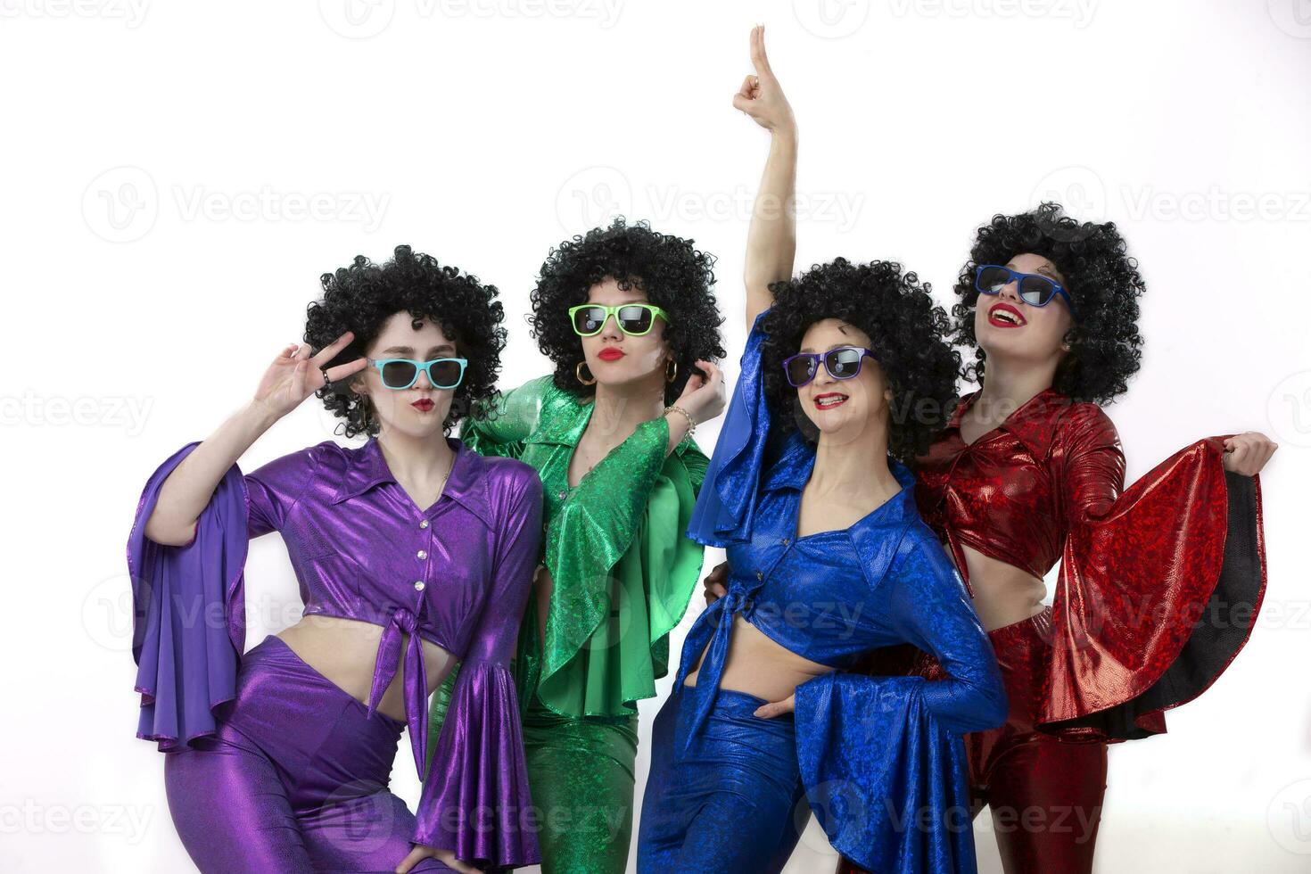 A group of girls in colorful flared suits and afro wigs pose against a white background. Disco style from the eighties or seventies. photo