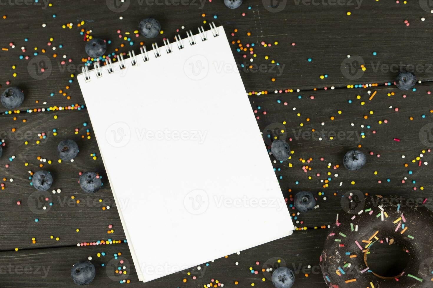 On a wooden background, a blank notebook, chocolate donuts and blueberries. Creative cuisine. photo