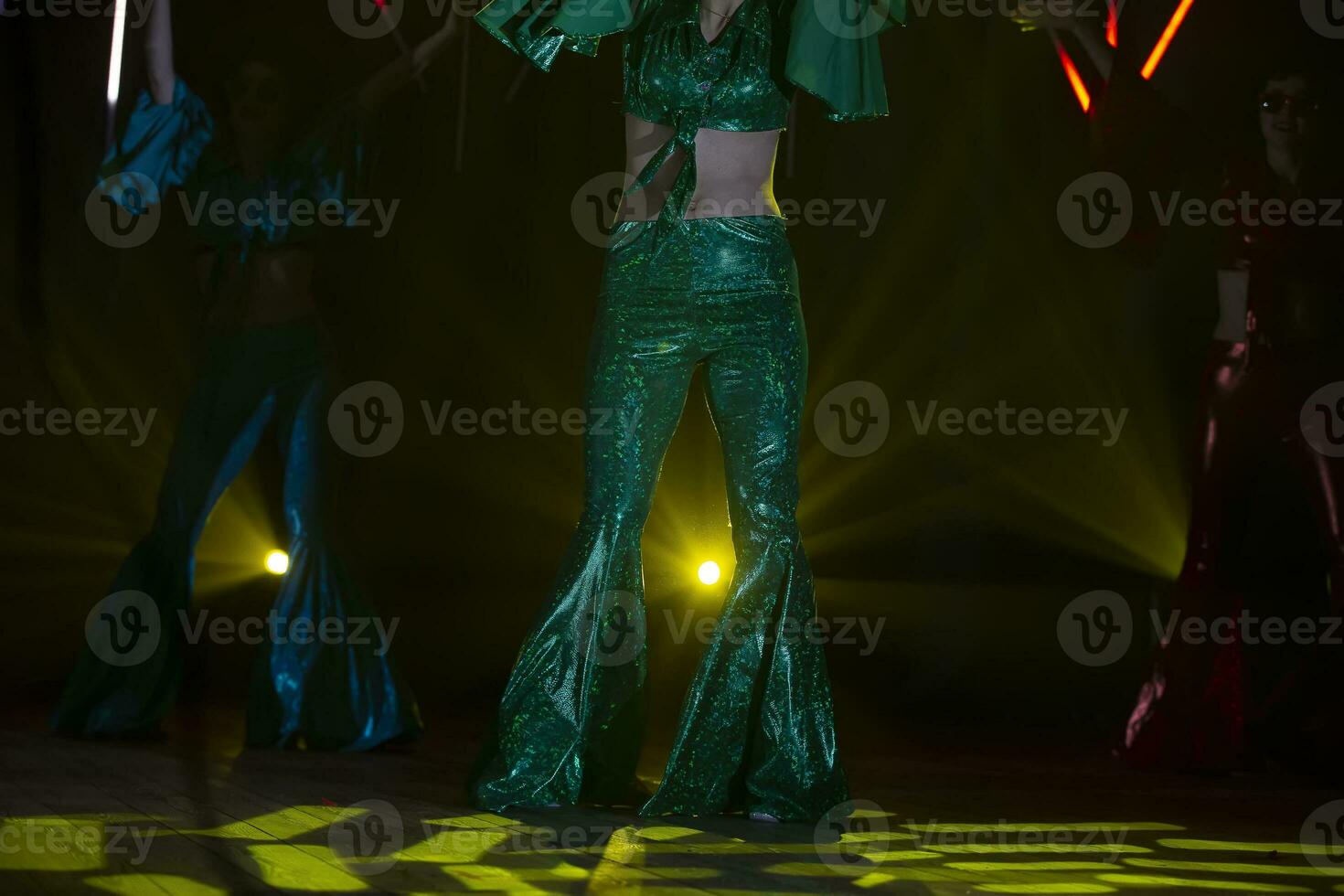 On the concert stage, illuminated by multi-colored beams, women's legs in 80s disco bell-bottoms. photo