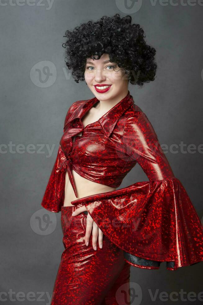 Vintage woman in afro wig and red disco costume on a gray background. Girl in the style of the seventies. photo
