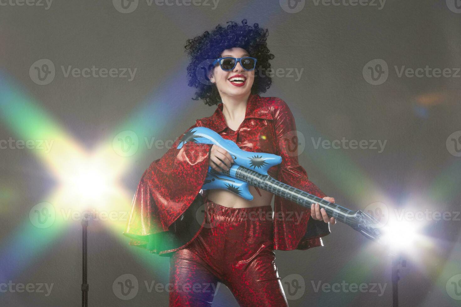 Cheerful woman in a red disco style stage costume holds a comic guitar in her hands. photo