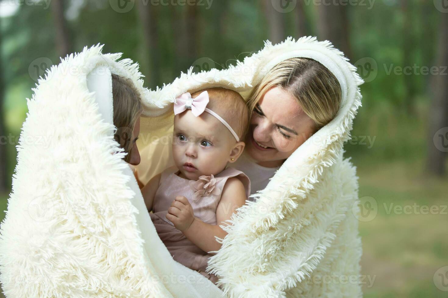 Two women hold a beautiful little girl in their arms. photo