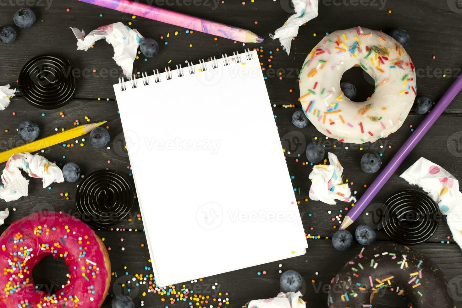 On a wooden background, a blank notebook with a pencil, colorful donuts and scraps of paper. Creative cuisine. photo