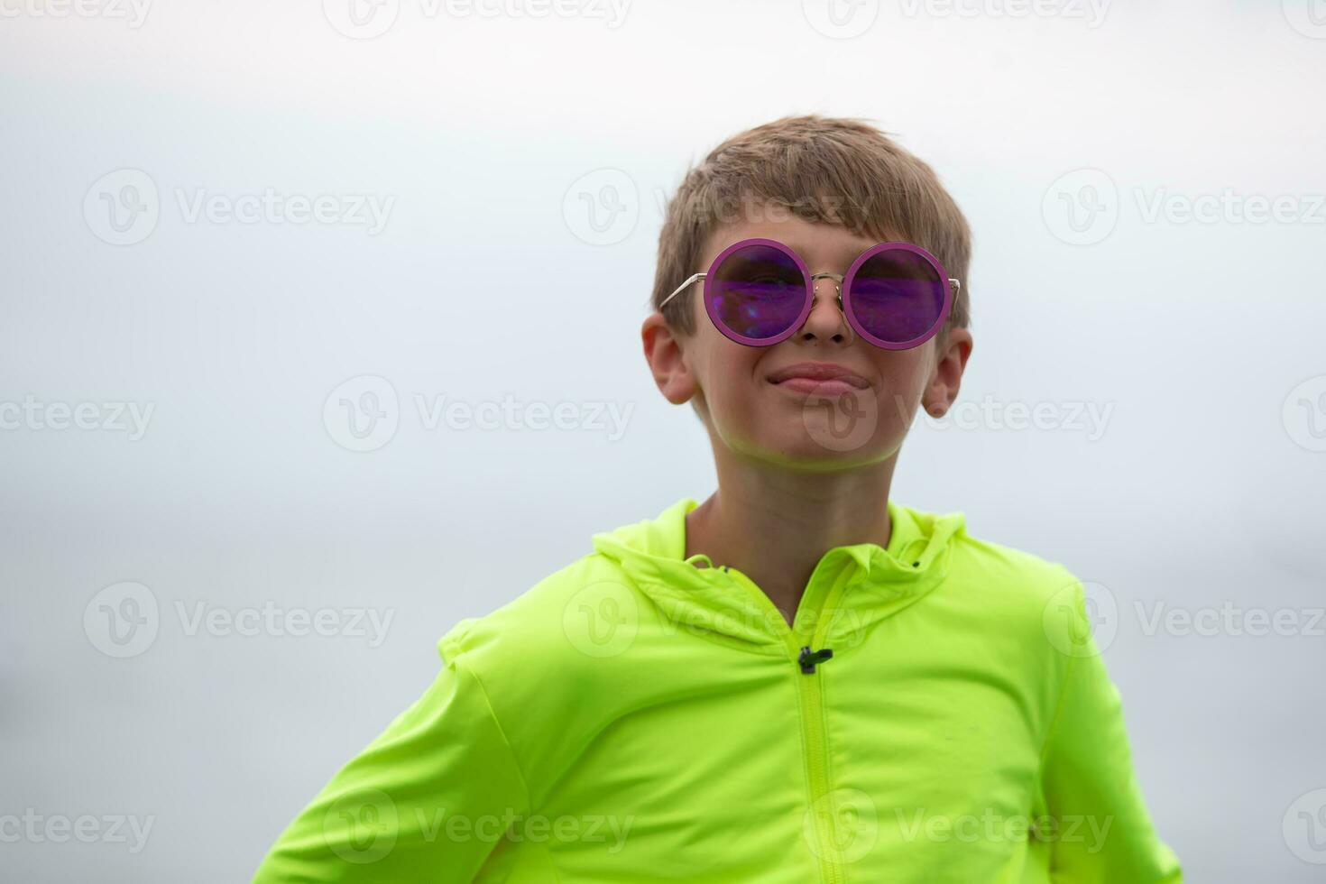 A handsome boy in a bright green sweater and purple sunglasses. Portrait of a happy ten year old boy. photo