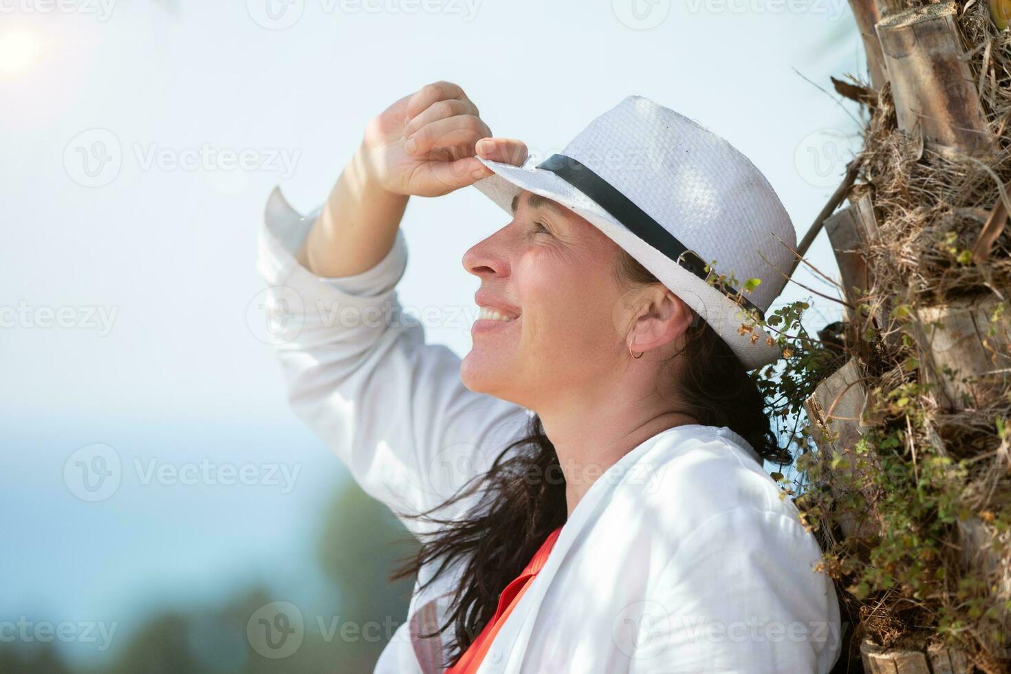 Profile of a happy woman near a tropical palm tree. Summer vacation or vacation for a middle-aged woman. photo