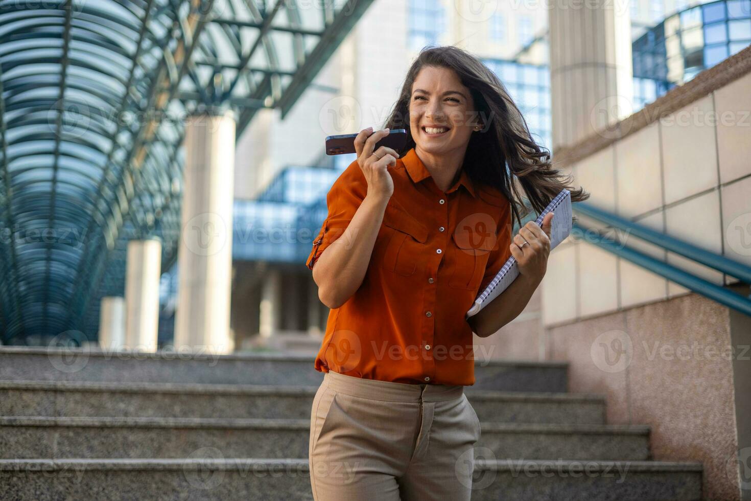 Smiling young business woman wearing suit standing on urban escalator using applications on cell phone, reading news on smartphone, fast connection, checking mobile apps outdoors. photo