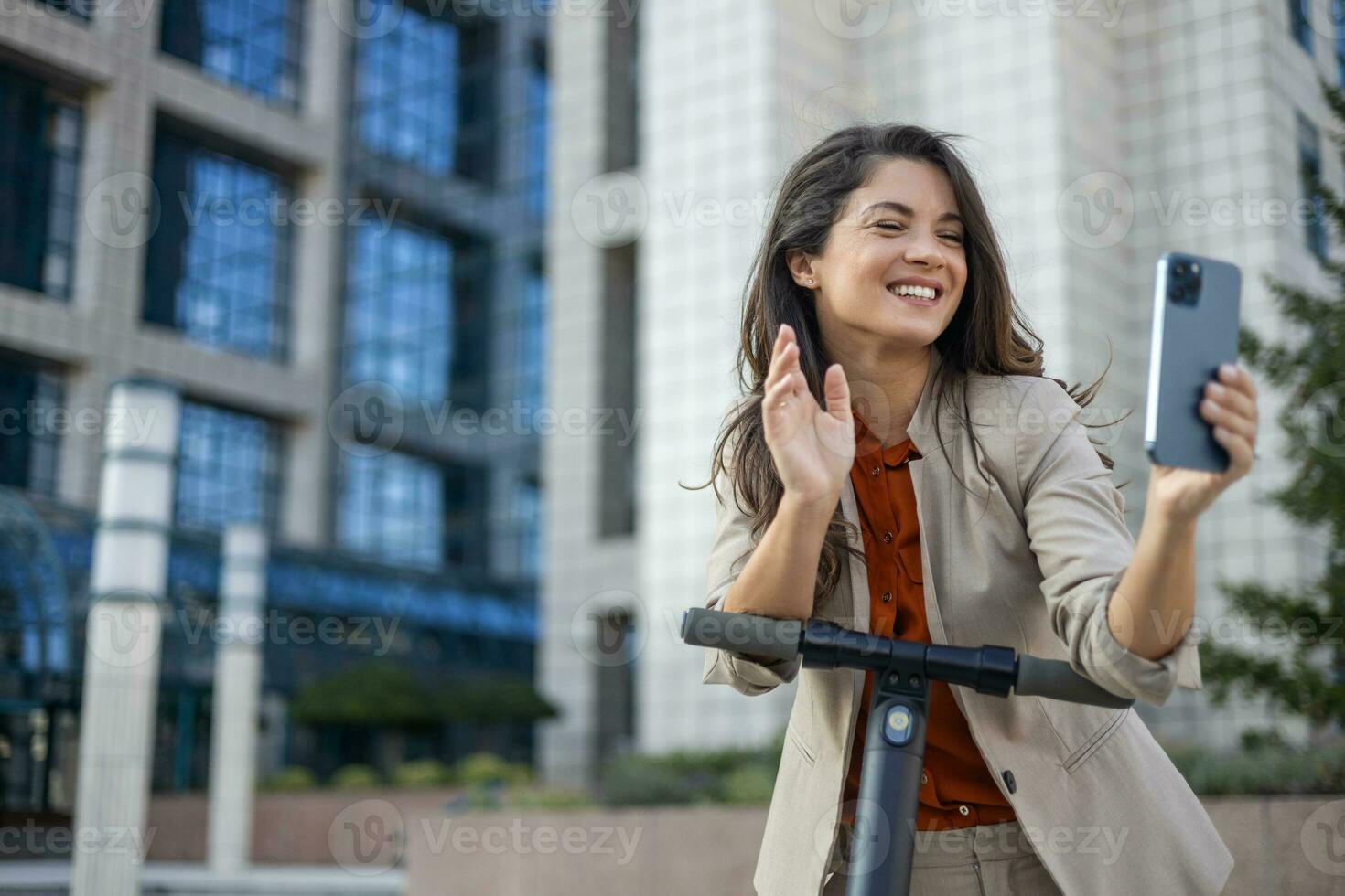 Female entrepreneur with smartphone while driving an electrical push scooter near business center on city street. Transportation environmental concept photo
