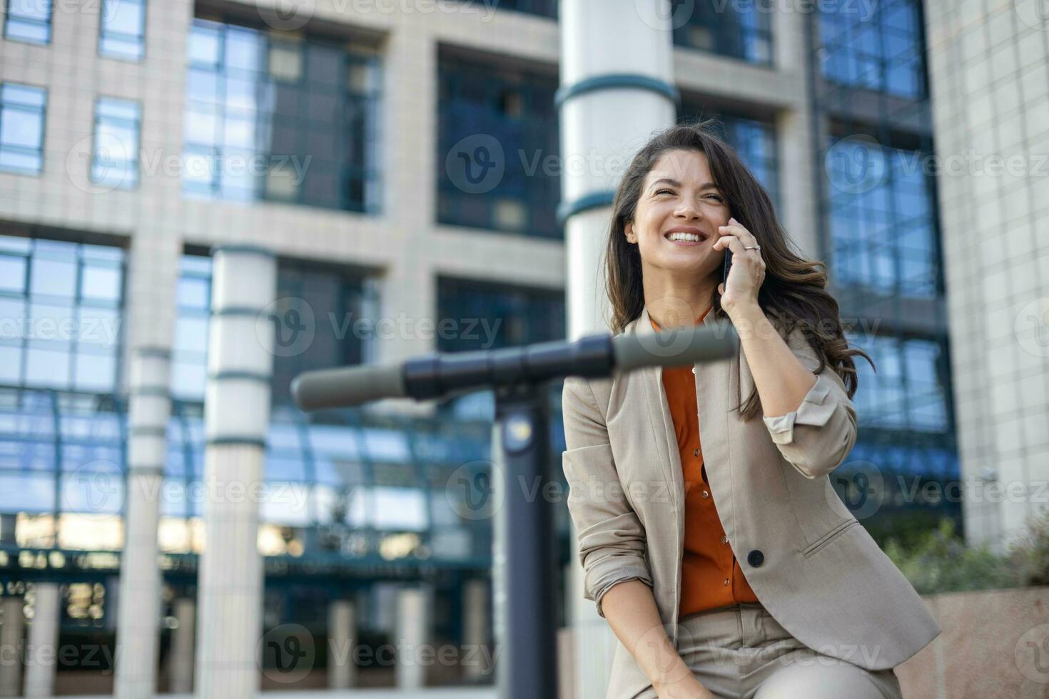 Female entrepreneur with smartphone while driving an electrical push scooter near business center on city street. Transportation environmental concept photo
