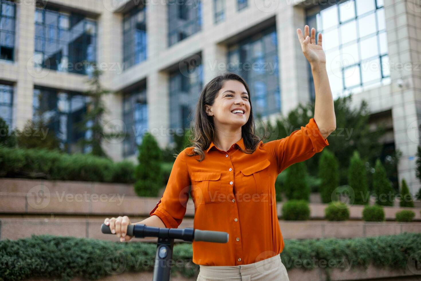 Young beautiful woman smiles and rides an electric scooter to work along office buildings. Ecological transportation concept. photo