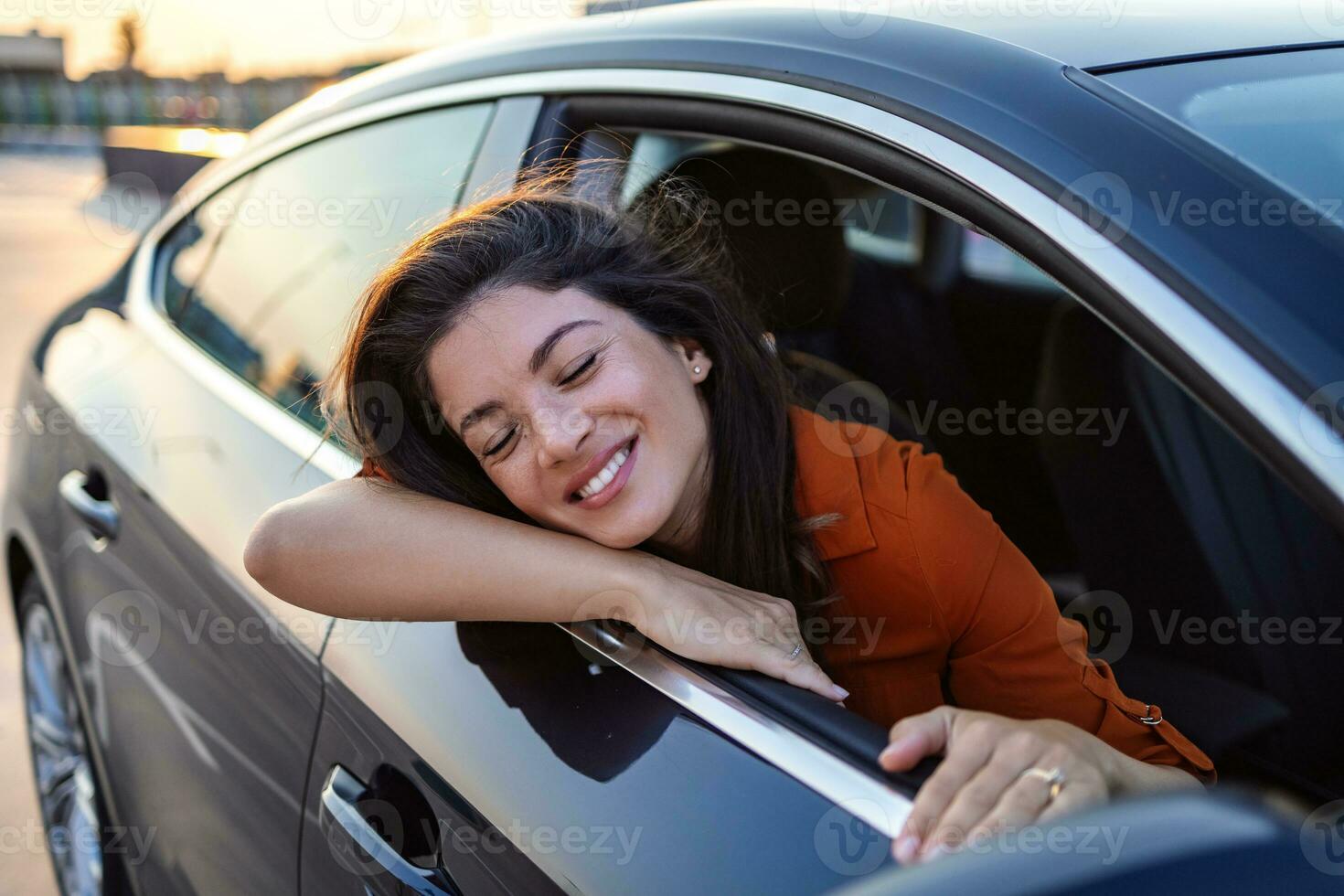 alegre joven hembra sentado en brillante coche en pasajero asiento y propensión fuera abierto ventana mientras disfrutando el paseo foto