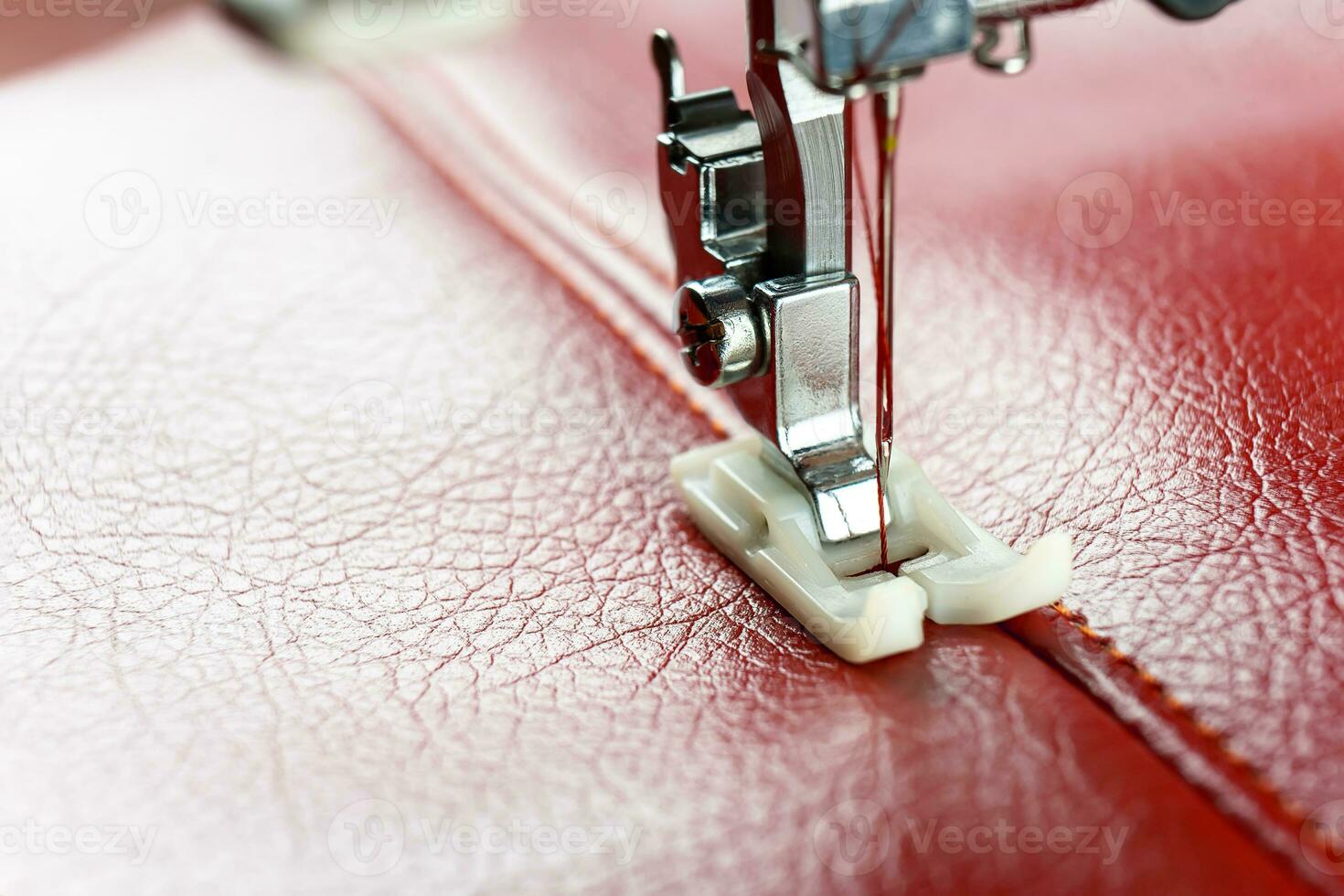 Modern sewing machine presser foot with a needle sews red leather photo