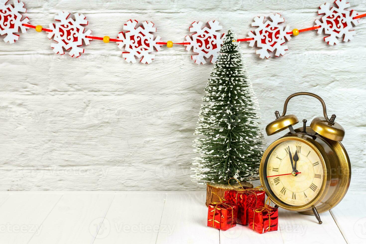 Decorative christmas tree, gift boxes and alarm clock on white wooden background. photo