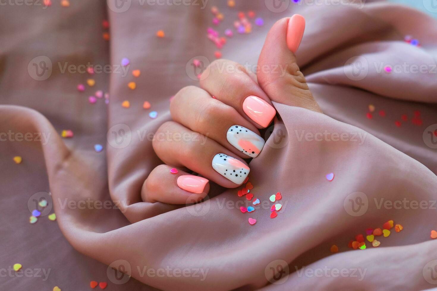 mujer - un mano con un hermosa manicura sostiene un seda tela en un antecedentes de destellos rosado tendencia, pulido el modelo en el uñas con gel polaco, goma laca. fiesta foto