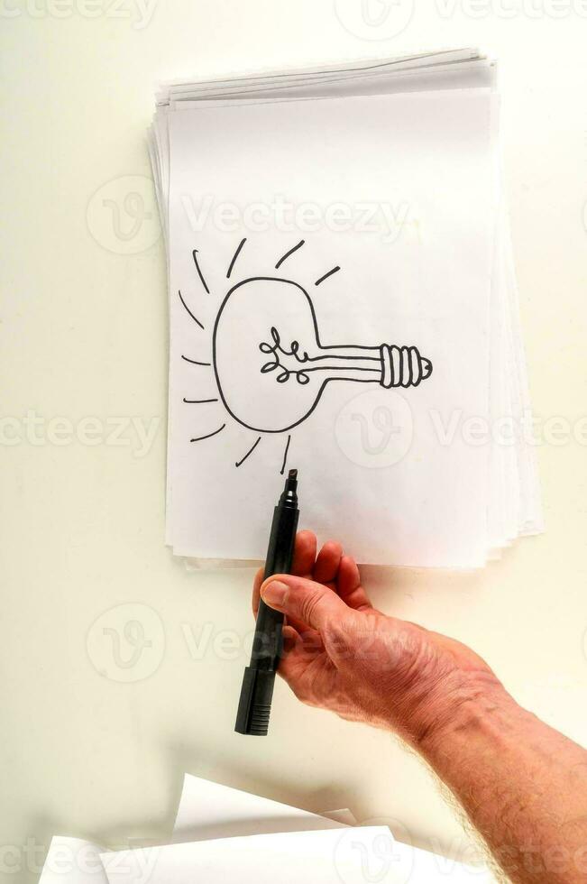 a hand holding a pen and drawing a light bulb photo