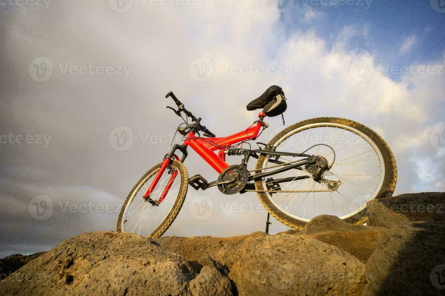 a red mountain bike is sitting on top of a rock photo