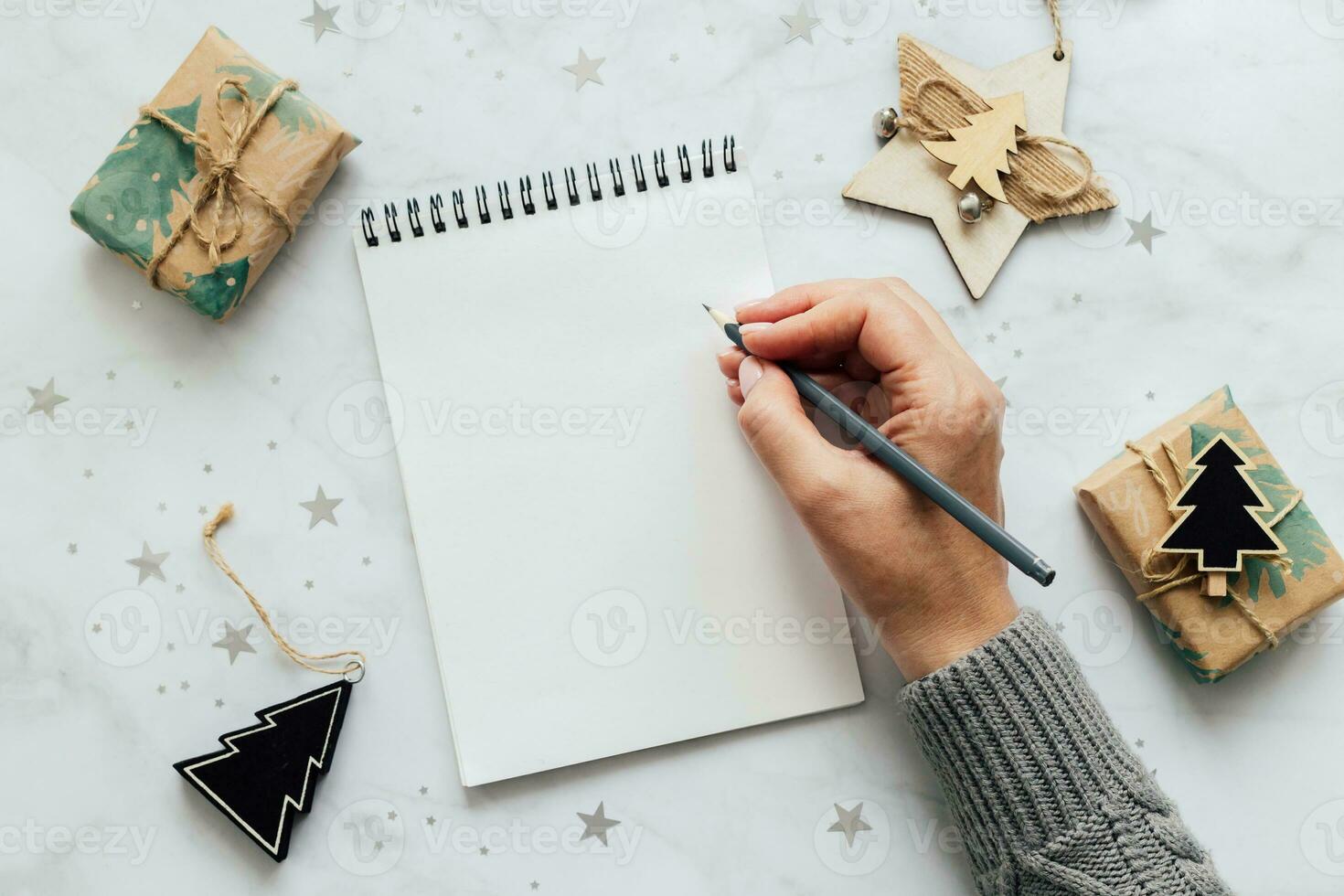 Female hand writing in a empty notebook. Festive decoration on table. Flat lay. New Year's plans and goals photo