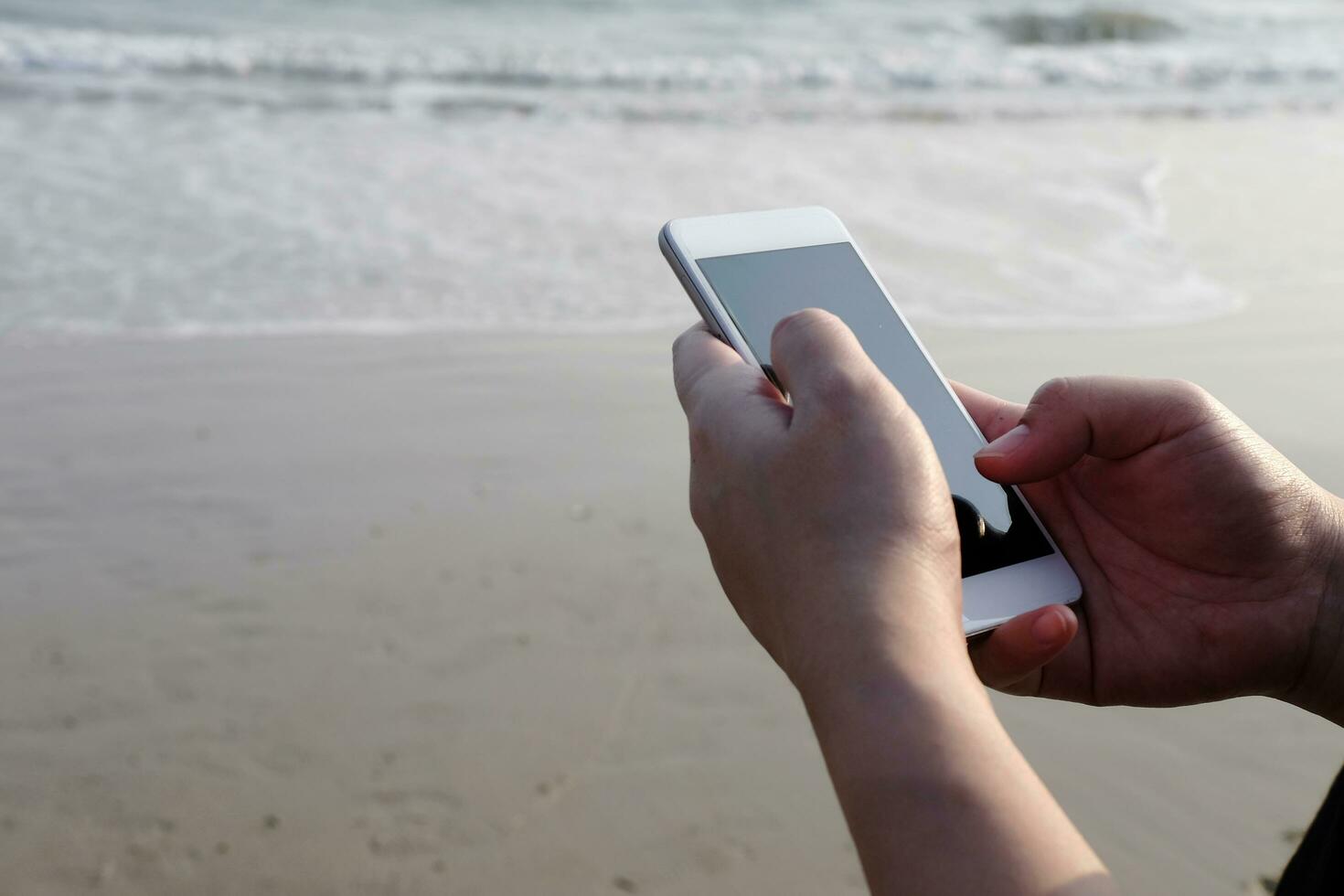 Closed up hand holding smartphone and touch screen for online with internet on the beach and seaside for business trip. Vacation and relaxation with technology on holiday concept photo