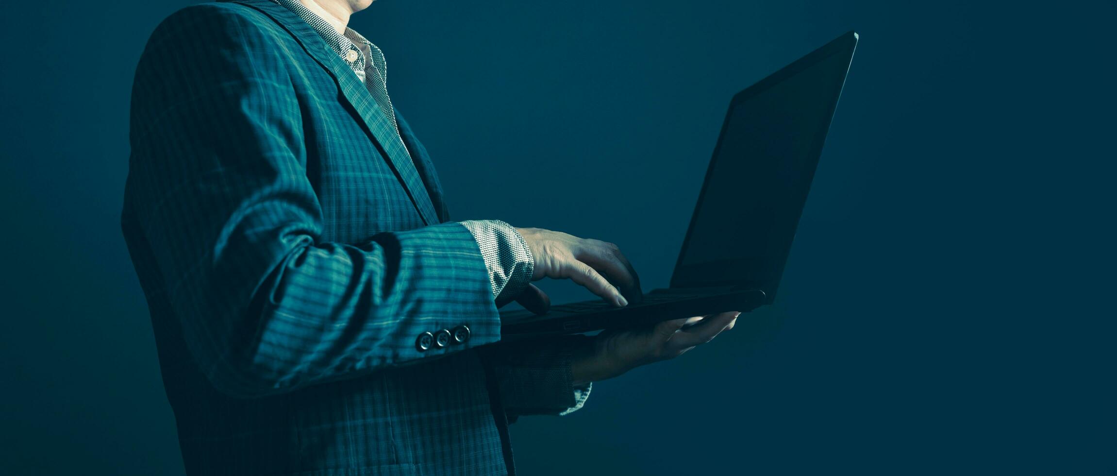 Businessman standing sideways holding and typing laptop computer. photo