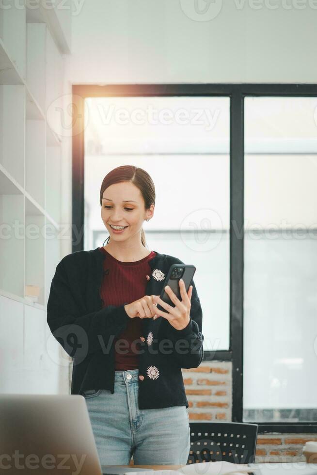 Attractive young woman talking on the smart phone and smiling while standing in office. photo