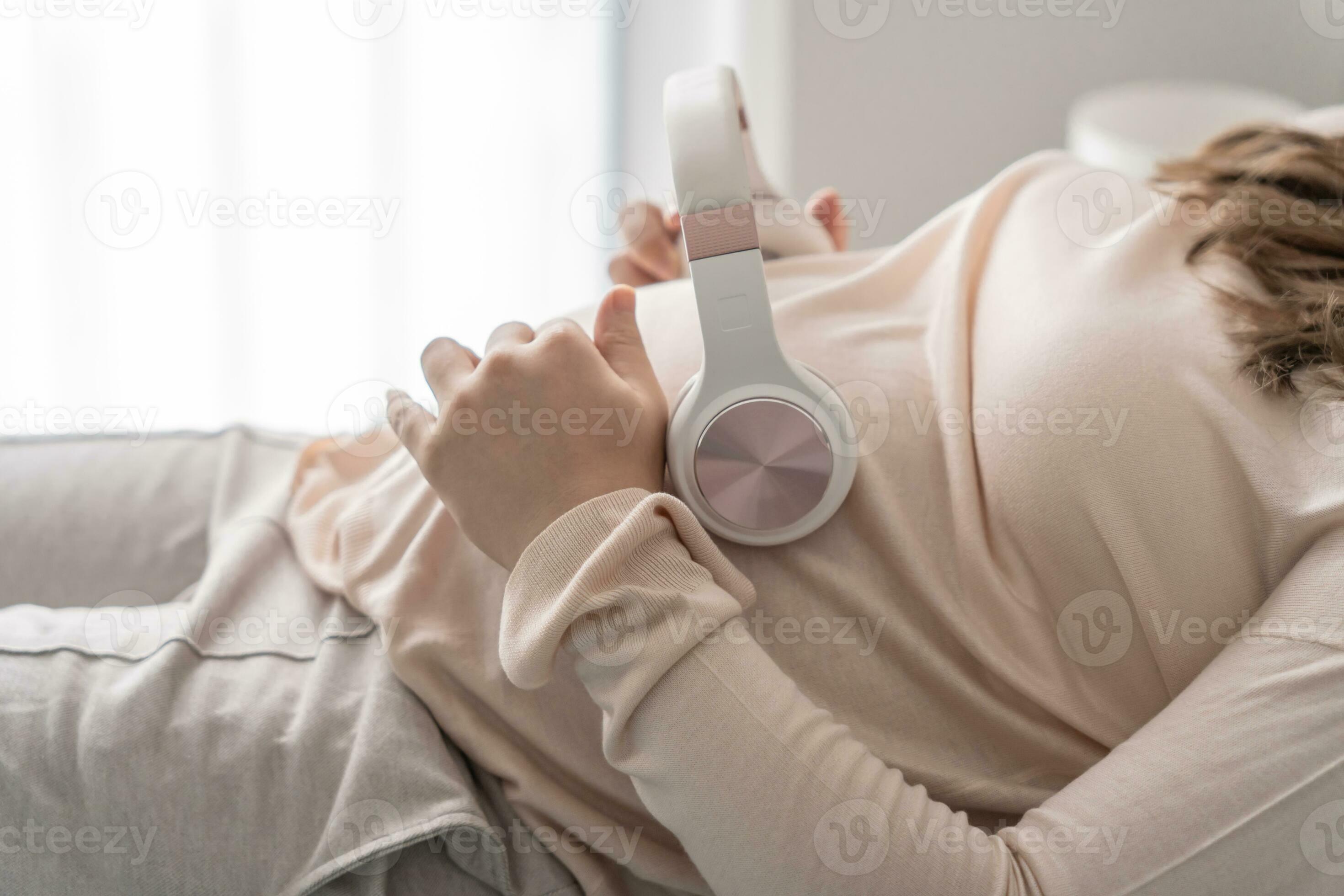 Pregnant asian woman holding headphone on belly playing music to her