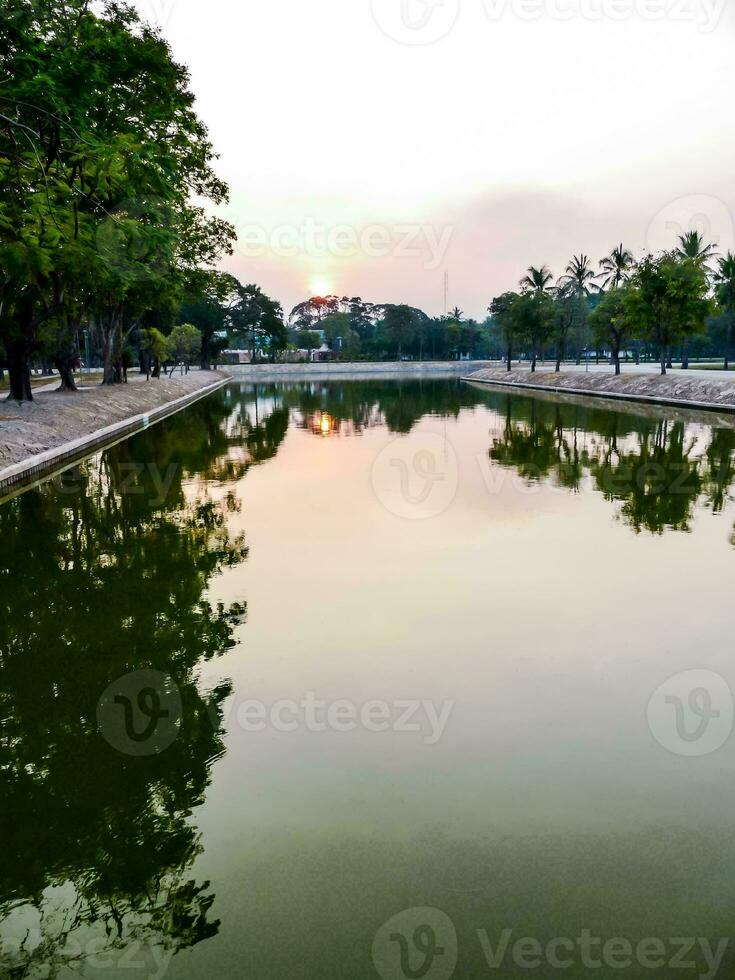 the sun sets over a pond in a park photo