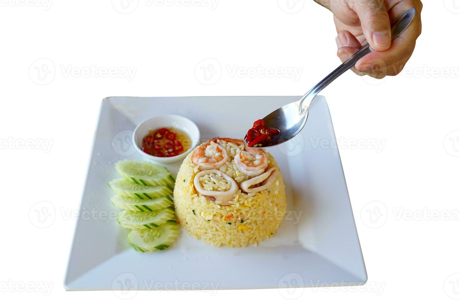 Hand holding a spoon with Chili and fish sauce poured over a plate of