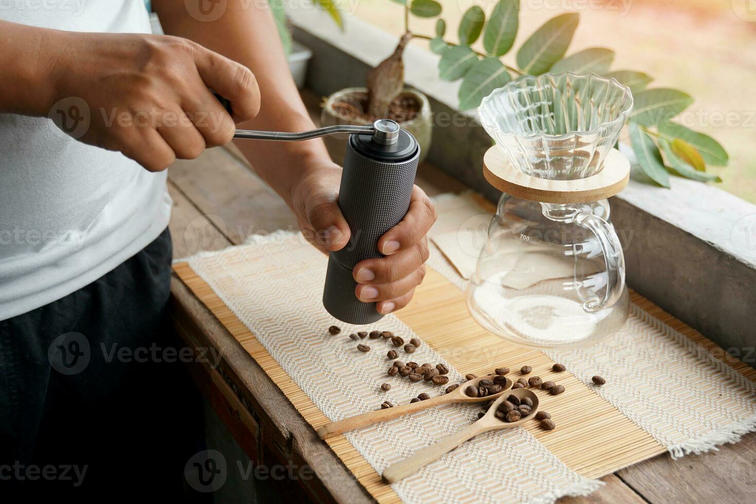 Asian man grinding coffee beans with grinder to easily drip black coffee at home, saving time and getting coffee that has a special aroma and taste. Soft and selective focus. photo