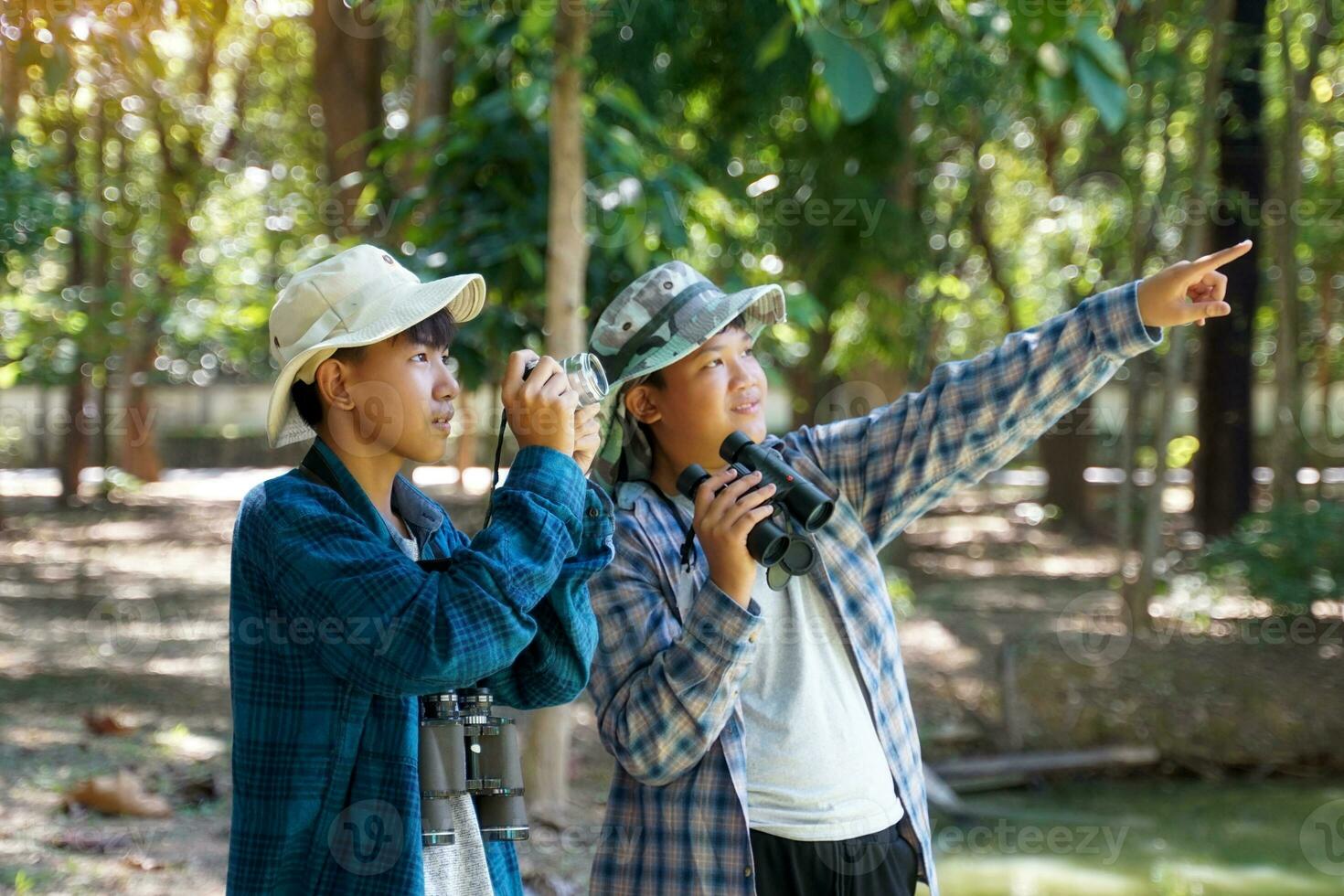 Two Asian boys use binoculars and a camera to study the local birds in a community forest. Soft and selective focus. photo