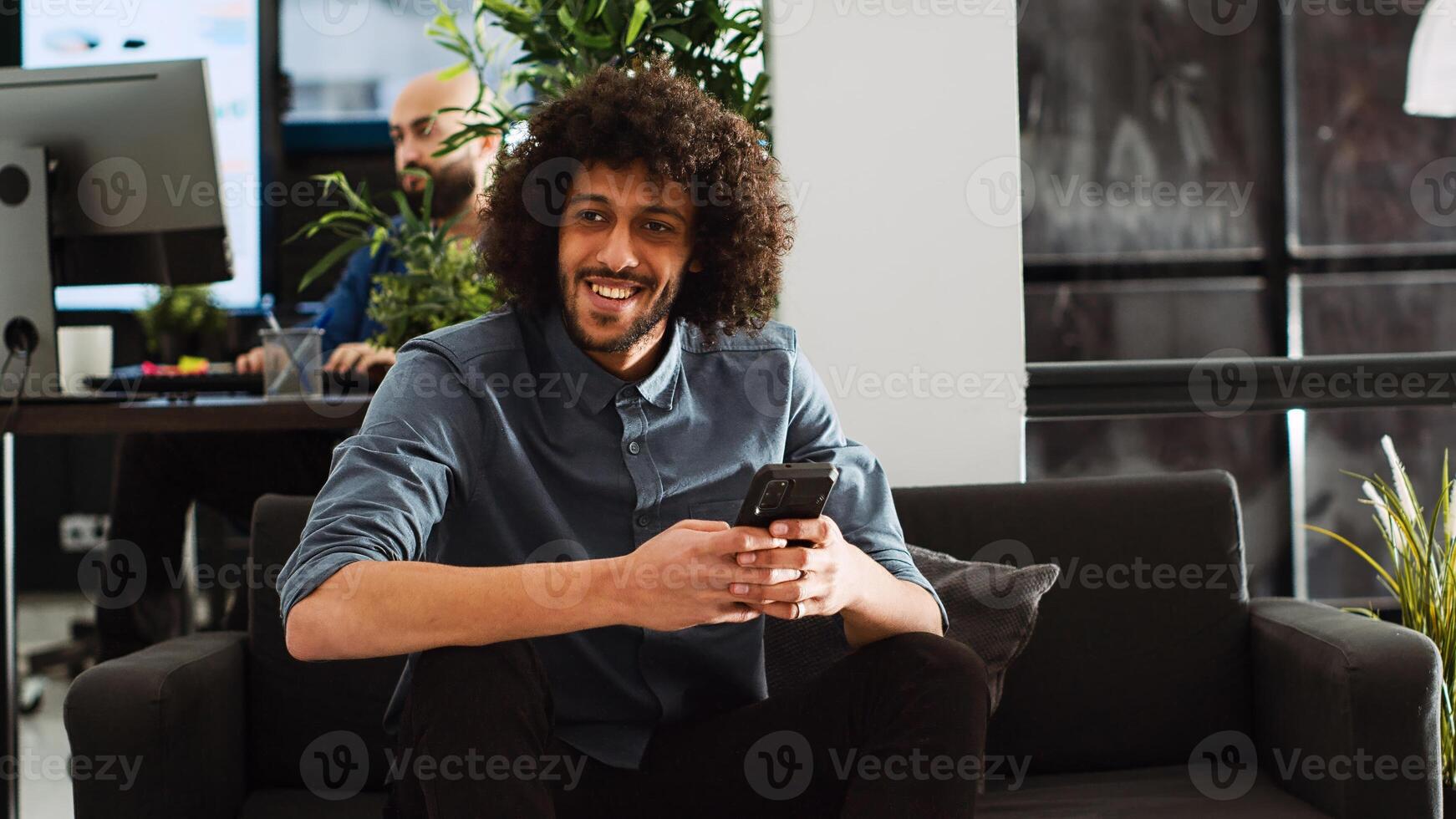 Company worker analyzing strategy on smartphone, working in open space office. Middle eastern employee using phone to do research for development project, entrepreneurship. Handheld shot. photo