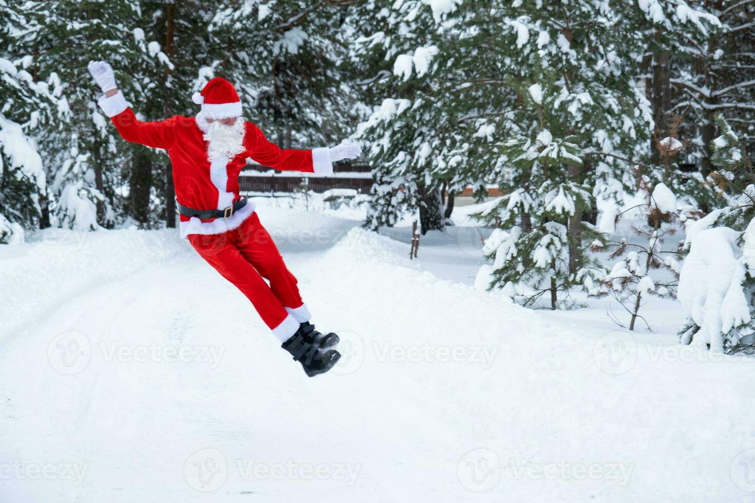 Santa Claus is having fun and funny jumping, outdoor in winter on a snowy road with pine trees. Celebrating Christmas and New Year. photo