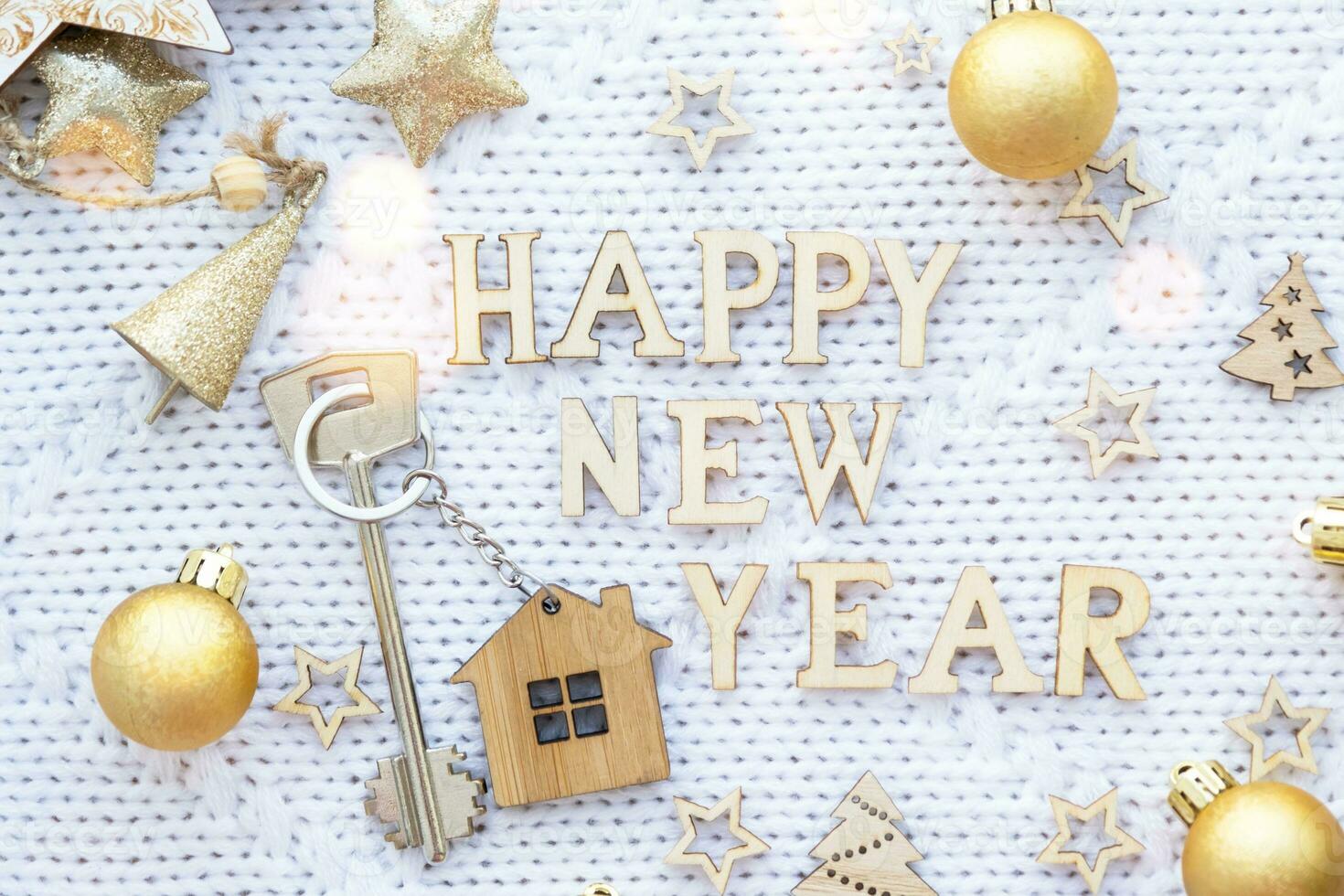 House key with keychain cottage on festive knitted background with stars, lights of garlands. Happy New Year wooden letters, greeting card. Purchase, construction, relocation, mortgage, insurance photo