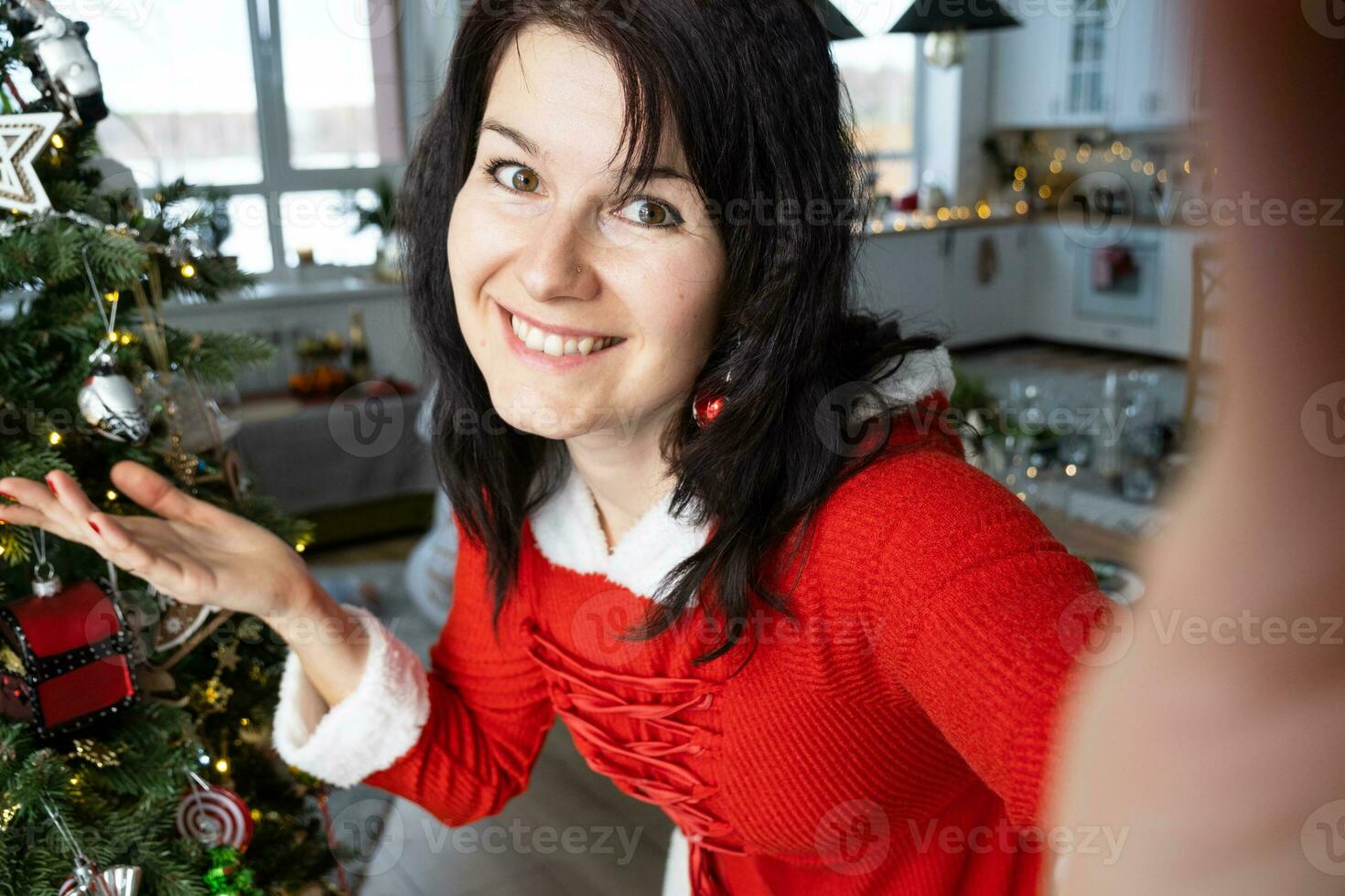 selfie retrato de un mujer en un rojo Papa Noel vestir en un hogar interior con un Navidad árbol y nuevo año decoración. preparación para el vacaciones, fiesta foto