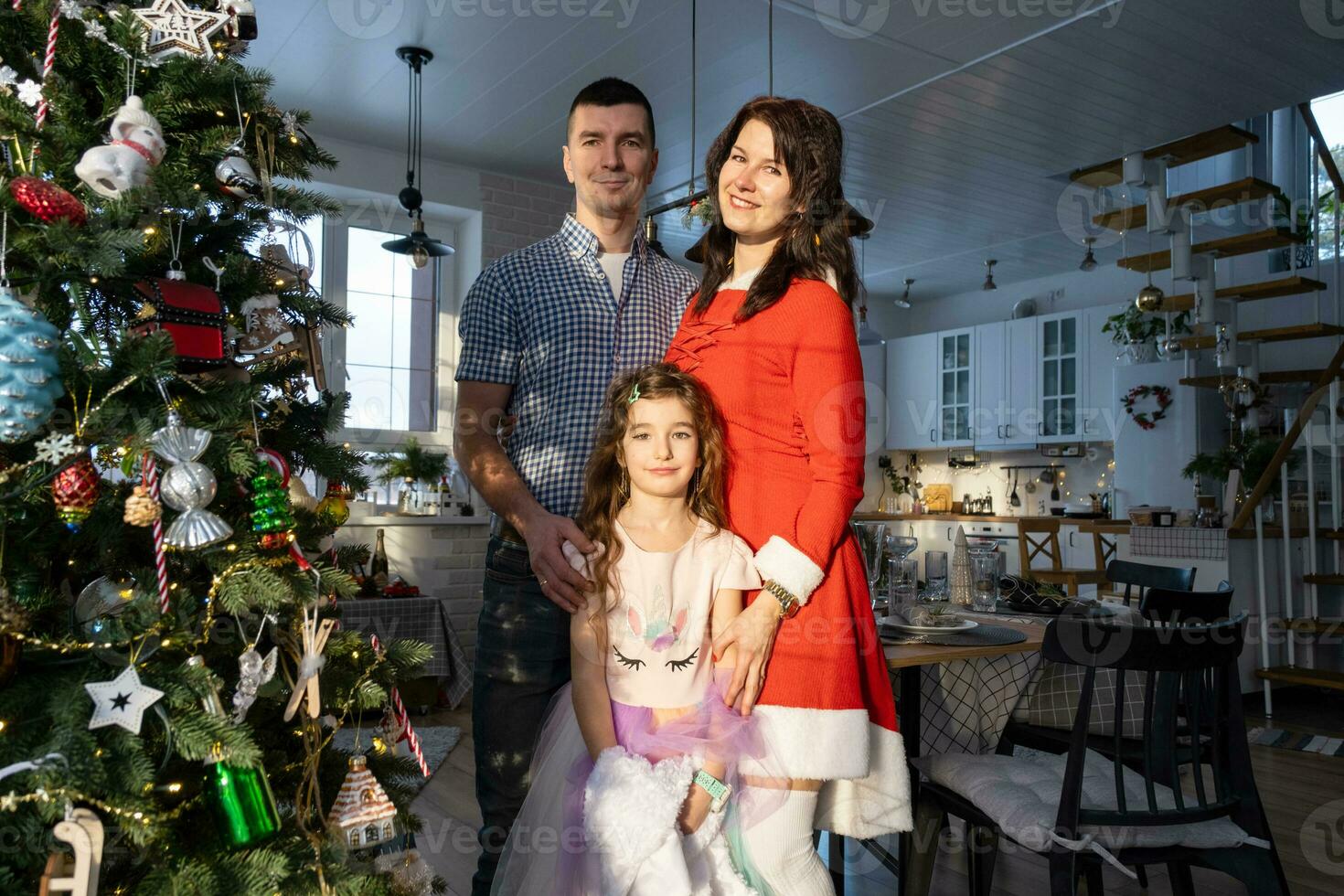 A traditional family of mom, dad and daughter near the Christmas tree in the interior of their house. Celebrating the New year with your family photo