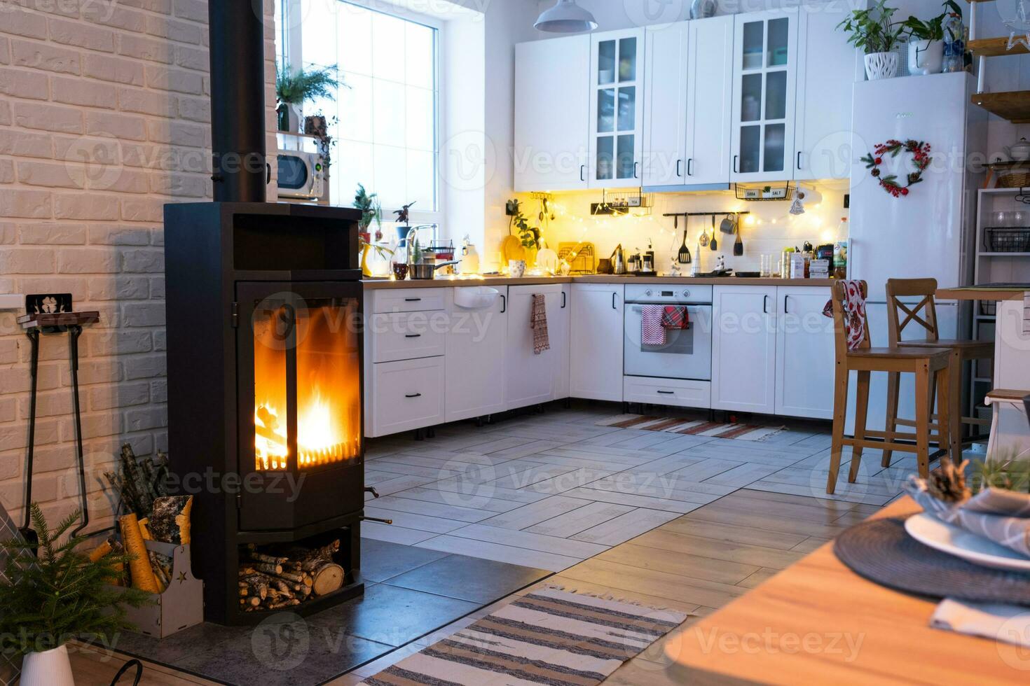 el interior festivo de la casa está decorado para navidad y año nuevo en estilo loft con estufa negra, chimenea, árbol de navidad. cálida sala de estudio con mesa puesta, madera quemada, acogedora y calefacción del hogar foto