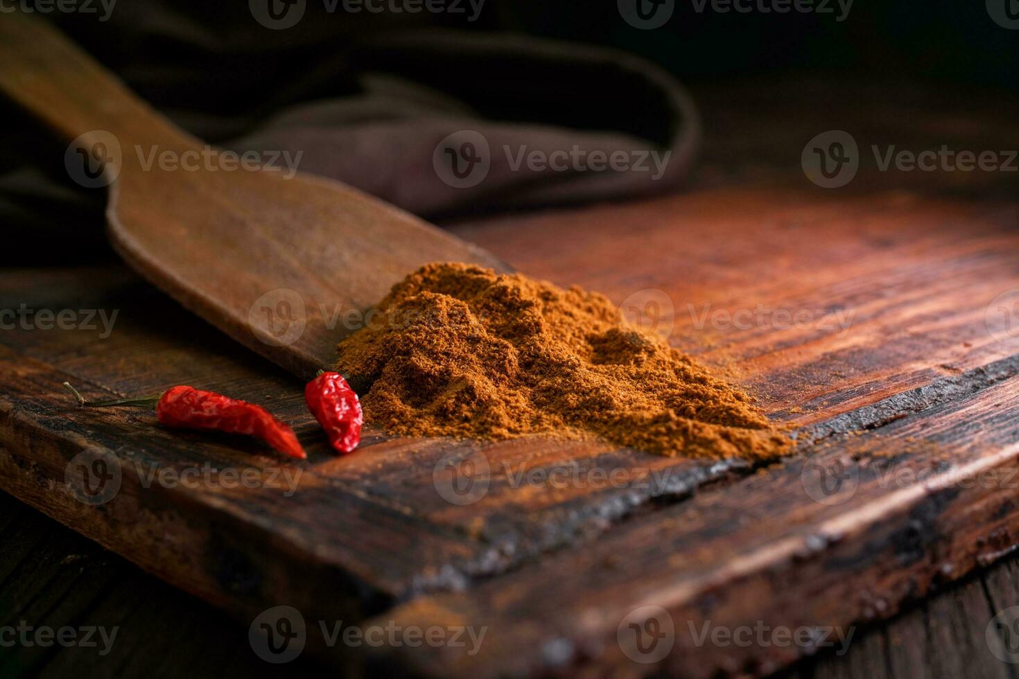 picante picado delicioso Condimento con rojo seco chile pimientos en un de madera espátula con un de madera tablero en un oscuro antecedentes foto
