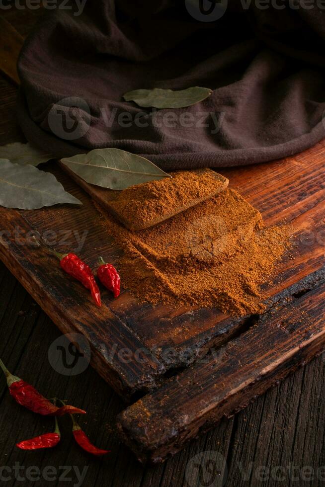 Spicy ground red spice with red dried chili peppers on a wooden brown table with leaves and a fabric photo