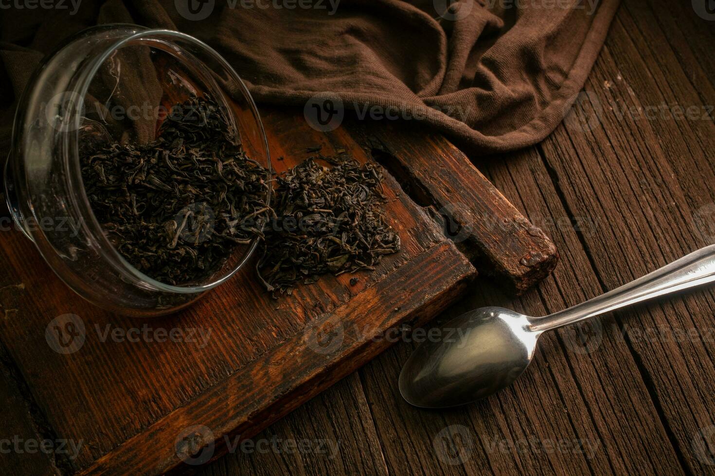 Green tea leaves in a glass jar with a spoon on a wooden brown board on a dark background. tea brewing time photo