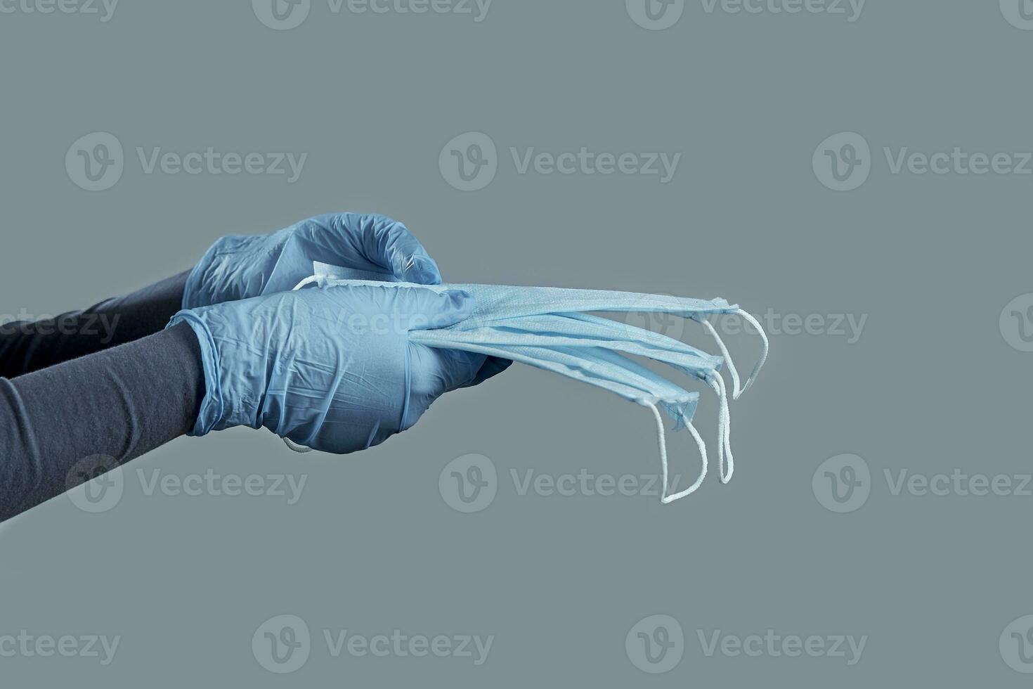 Hands in disposable gloves holding medical mask on a gray background. Photo with copy space.