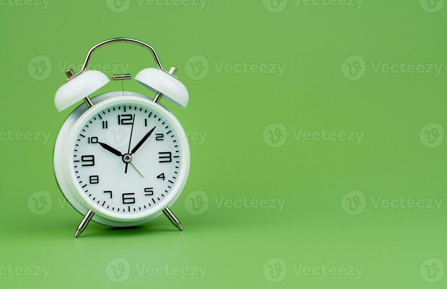 White alarm clock tells time working with time importance of time punctuality White clock on a green background photo