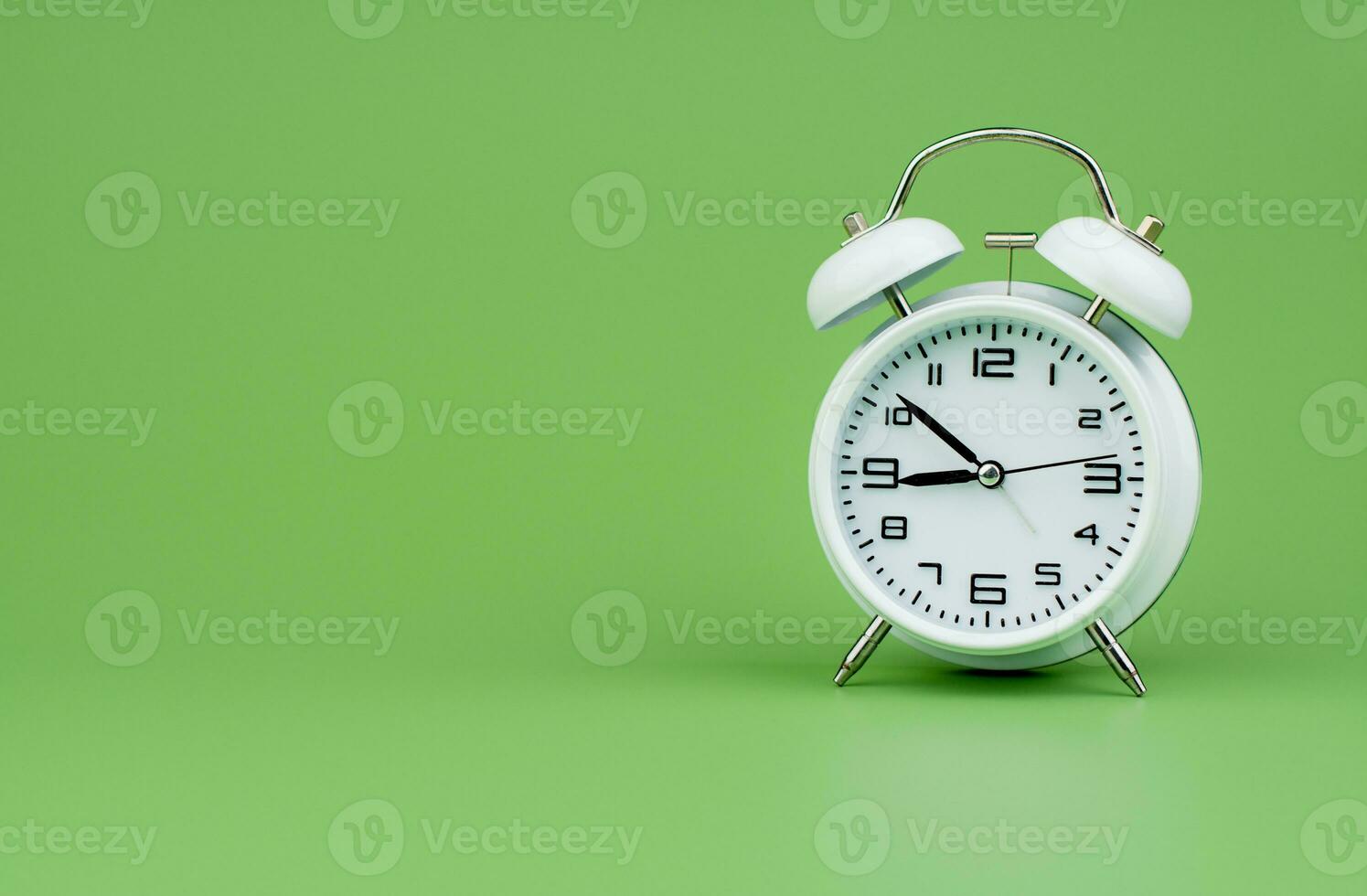 White alarm clock tells time working with time importance of time punctuality White clock on a green background photo