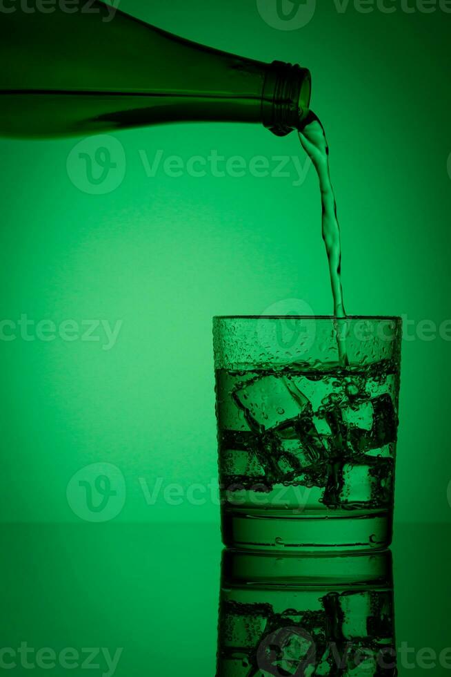 beautiful bottle with water and glass with ice and water on a green background photo