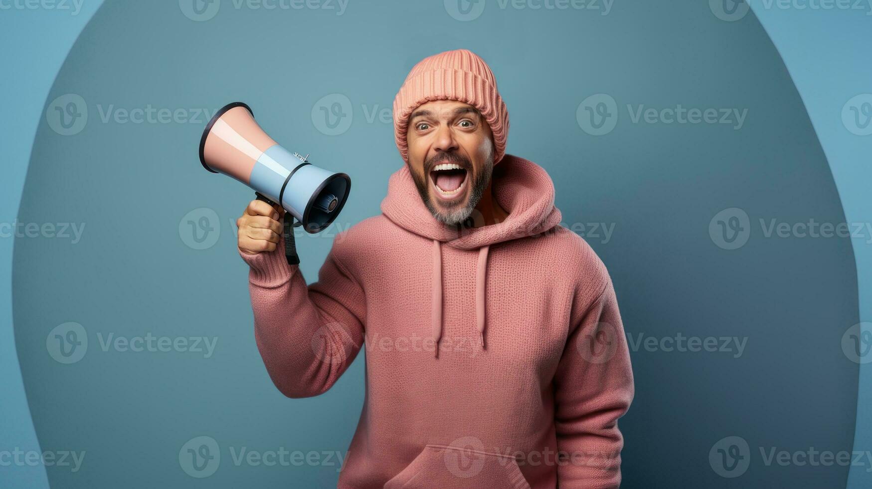 Happy man in pink hoodie and winter hat with megaphone on blue background. photo