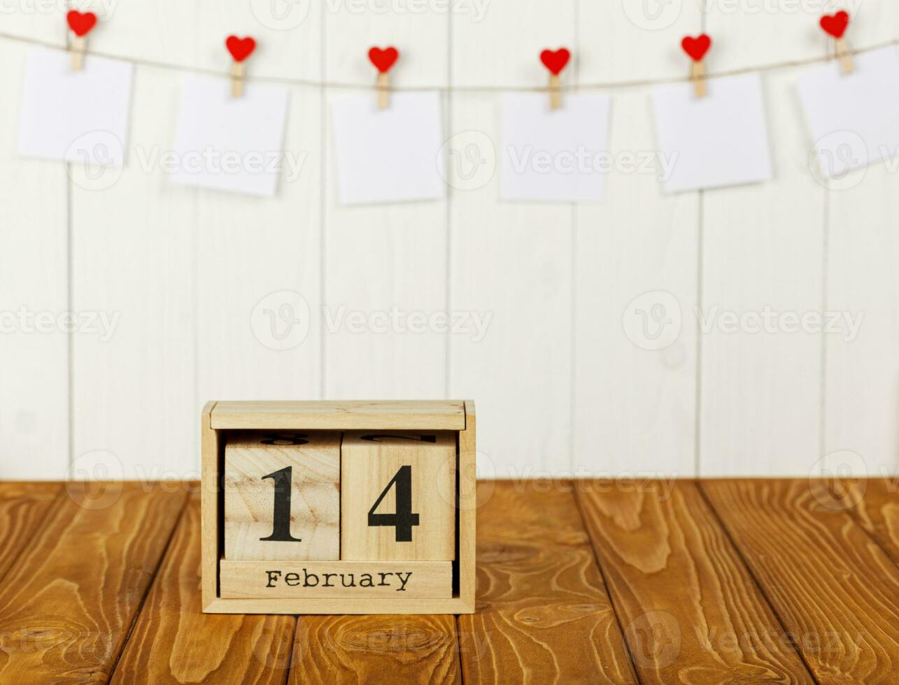 blanco piezas de papel en pinzas para la ropa con un corazón en un de madera fondo, calendario febrero 14 foto